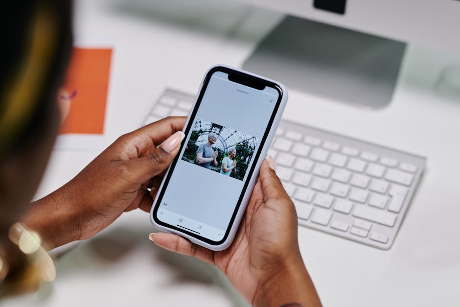 A person holding a smartphone viewing photos indoors near a keyboard.